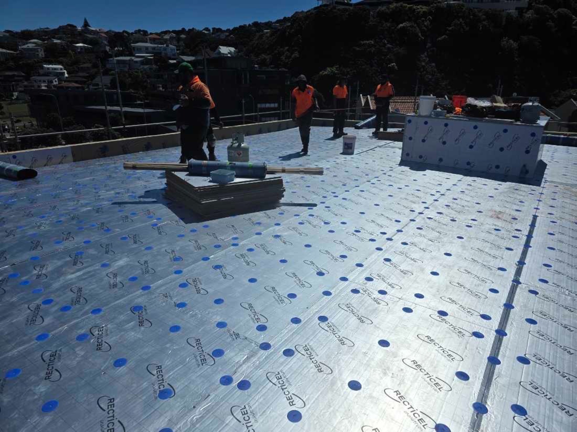 Highrise crew laying insulation board on a clifftop roof above the coast